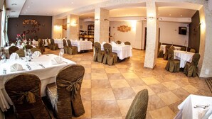 A restaurant with multiple round tables set for dining, each with white tablecloths and chairs with brown covers. - Hotel Logos (Gdansk)