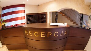 A reception desk with a curved design, a large American flag, and a wine rack. - Hotel Logos (Gdansk)