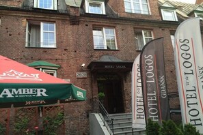 Ein Hotel namens Hotel Logos mit Ziegelaußenwand, einem grünen Vordach und einem Schild mit den Zimmernummern 26/28.