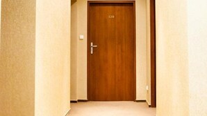 A hotel corridor with a wooden door marked "120", carpeted floors, and recessed ceiling lights. - Hotel Logos (Gdansk)