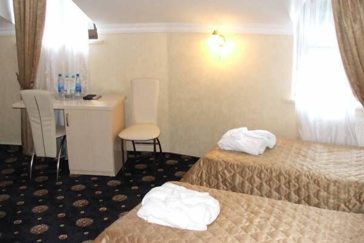 A hotel room with a desk, two beds, a chair, and a window with curtains.