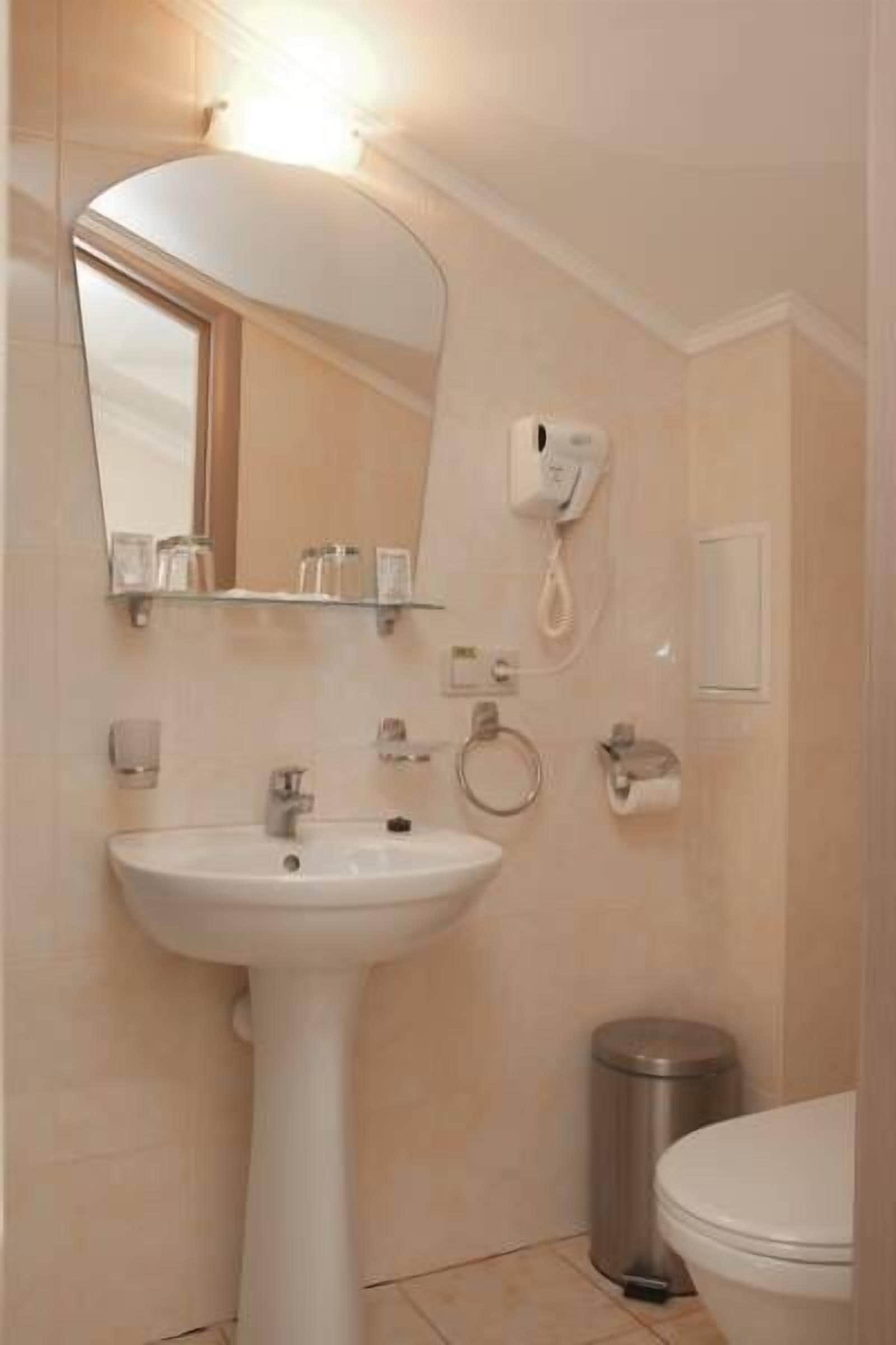 A bathroom with a pedestal sink, a mirror, a telephone, and a toilet.
