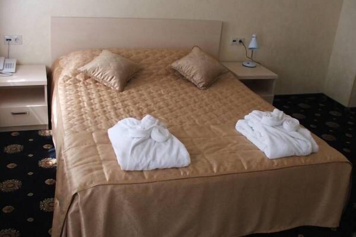 A neatly made bed with two pillows, a bedside table with a lamp, and a phone.