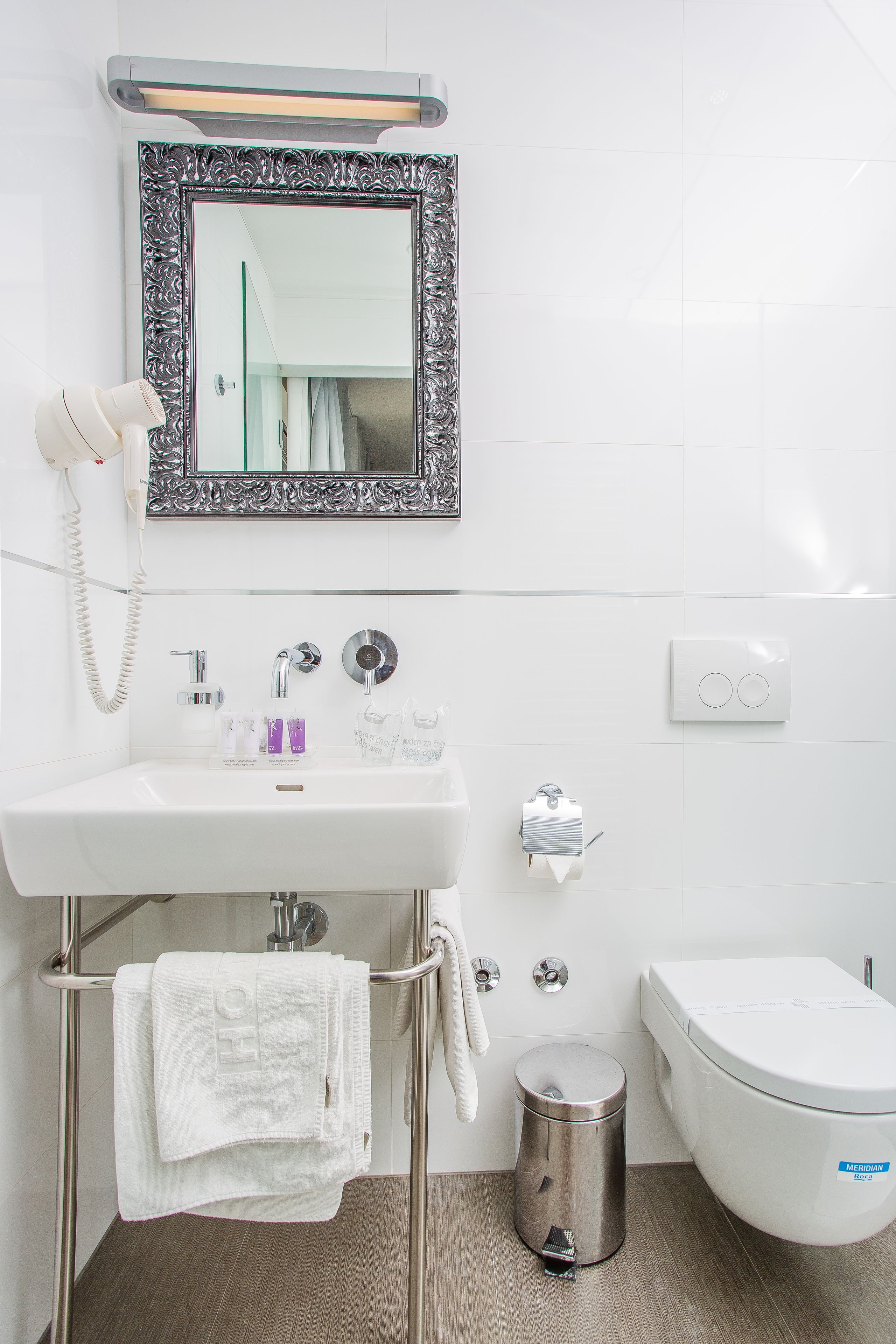 A modern bathroom with a white sink, a mirror with an ornate frame, a hairdryer, and a toilet.