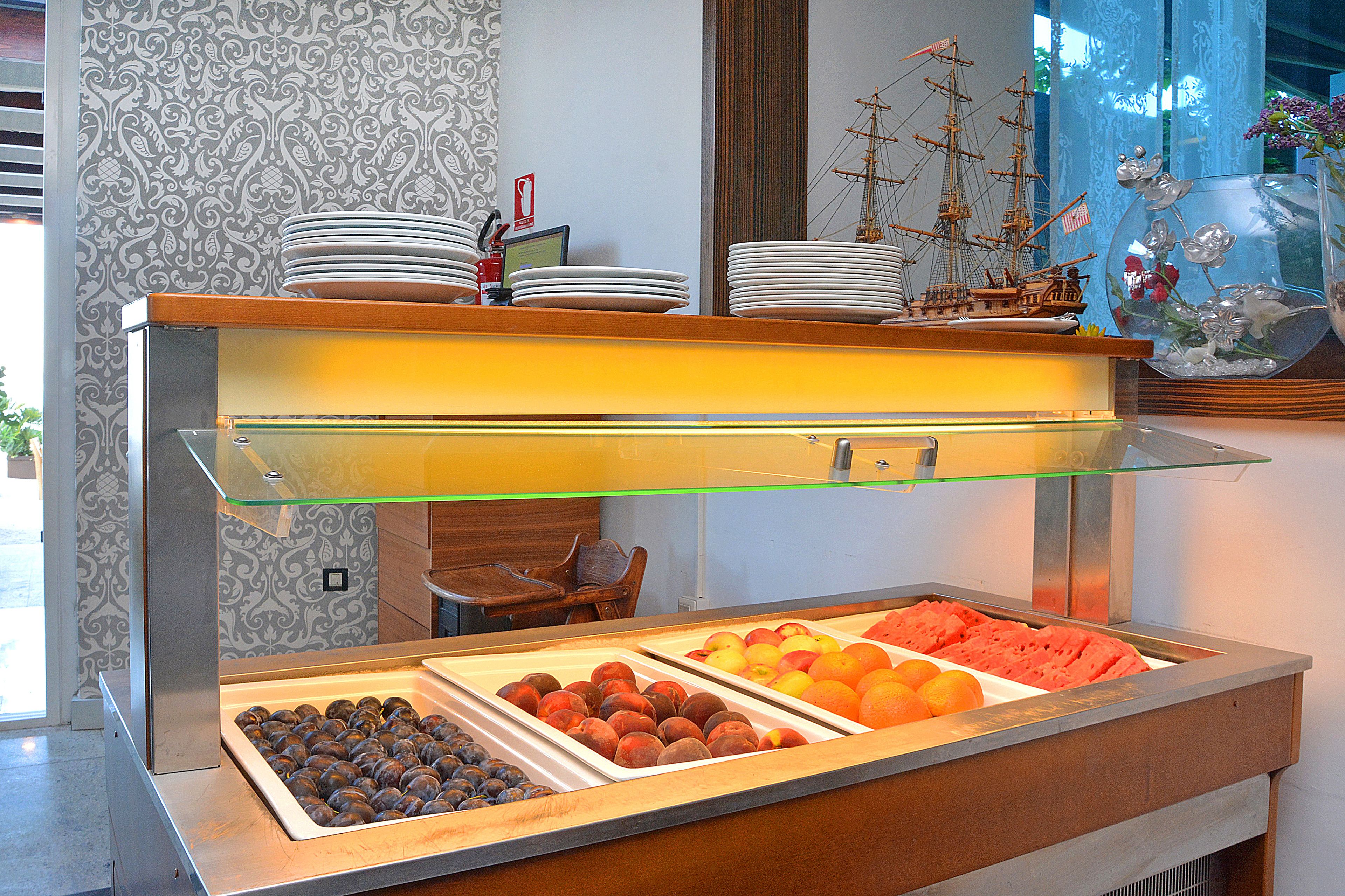 Un bufé con diversas frutas y bollería, un modelo de barco y un jarrón de vidrio decorado con flores.