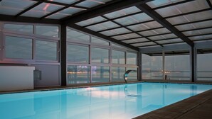 Piscina interna com vista para o horizonte urbano através de amplas janelas.