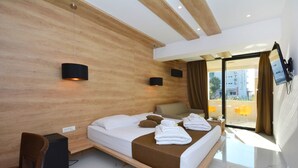 Quarto de hotel moderno com parede de destaque em madeira, uma cama grande com colcha marrom, uma escrivaninha com cadeira e vista para a cidade pela porta de vidro.