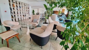Uma área de estar moderna com assentos, uma mesa de centro de vidro e uma estante repleta de objetos diversos.