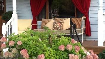 A porch with a bench, red curtains, and a flower bed with pink hydrangeas.