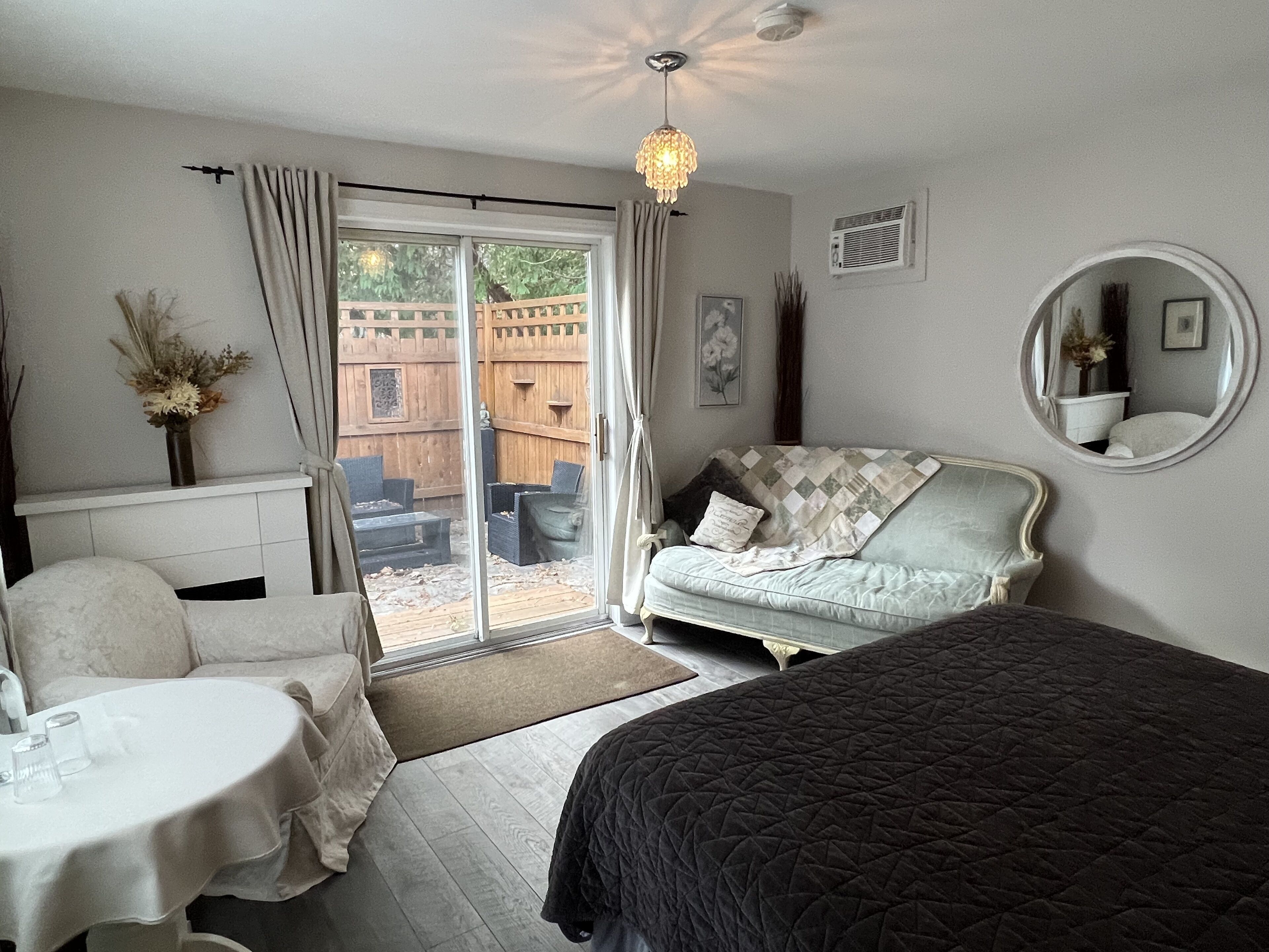 A bedroom with a bed, a sofa, a table, and a sliding glass door leading to an outdoor area.
