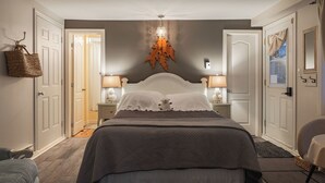 A bedroom with a large bed, two bedside lamps, a hanging light fixture, and a door with a mirror. -  Auberge Old Chelsea (Chelsea)