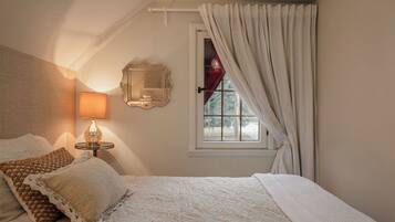 Een slaapkamer met een bed, een bedlamp, een spiegel en een raam met gordijnen.