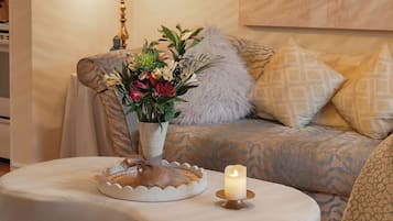 Un salón acogedor con un sofá estampado, un jarrón decorativo con flores, una vela sobre una mesita y un cojín con textura.