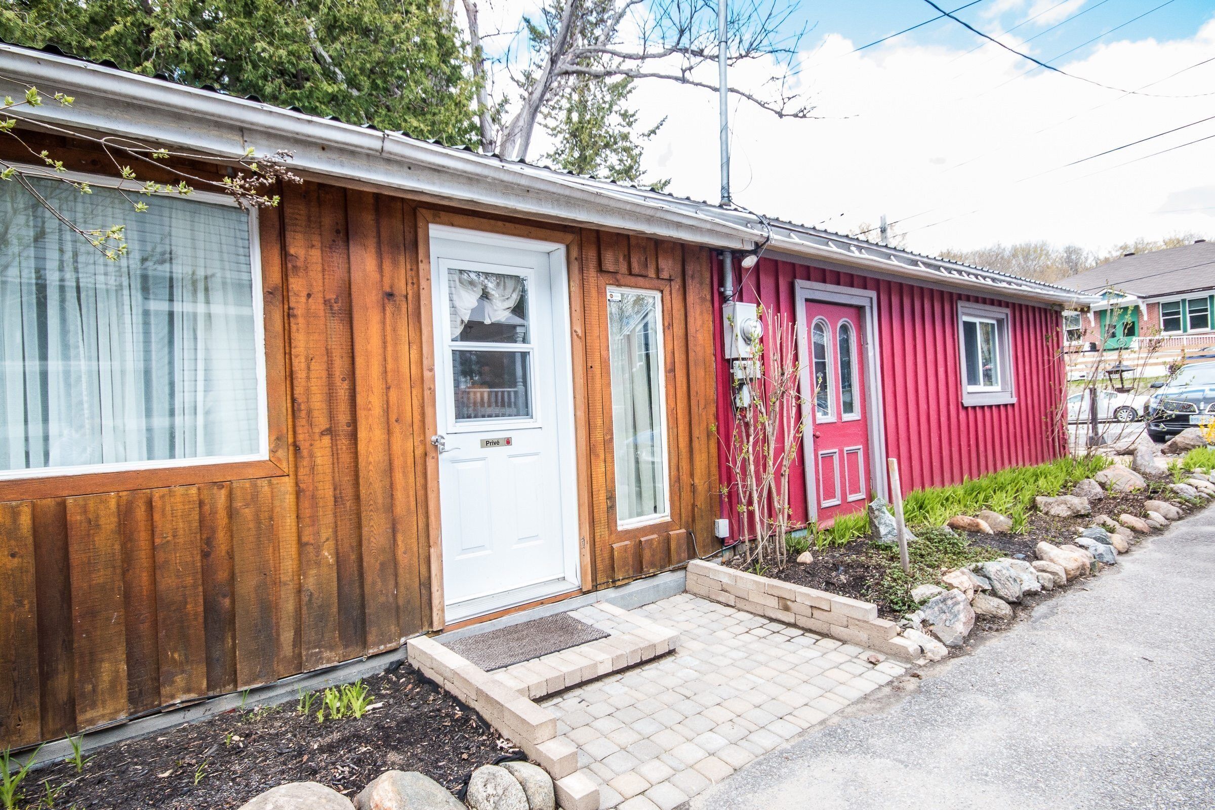 A wooden house with a red door and a white door, a small front porch, and a driveway.