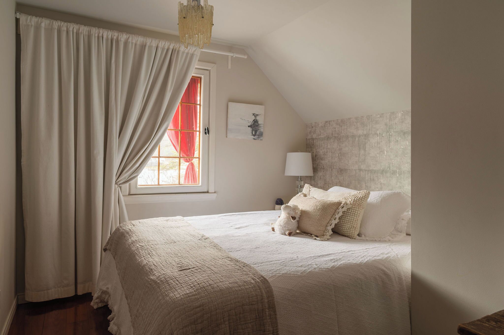 Un dormitorio con una cama grande, una ventana con cortinas rojas, una lámpara de pared y un aplique de techo.