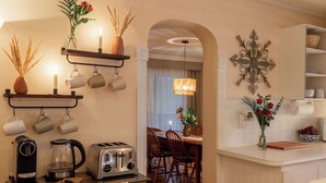 A kitchen with a coffee maker, toaster, and kettle on the counter, a dining area with chairs and a table, and a decorative wall piece. -  Auberge Old Chelsea (Chelsea)