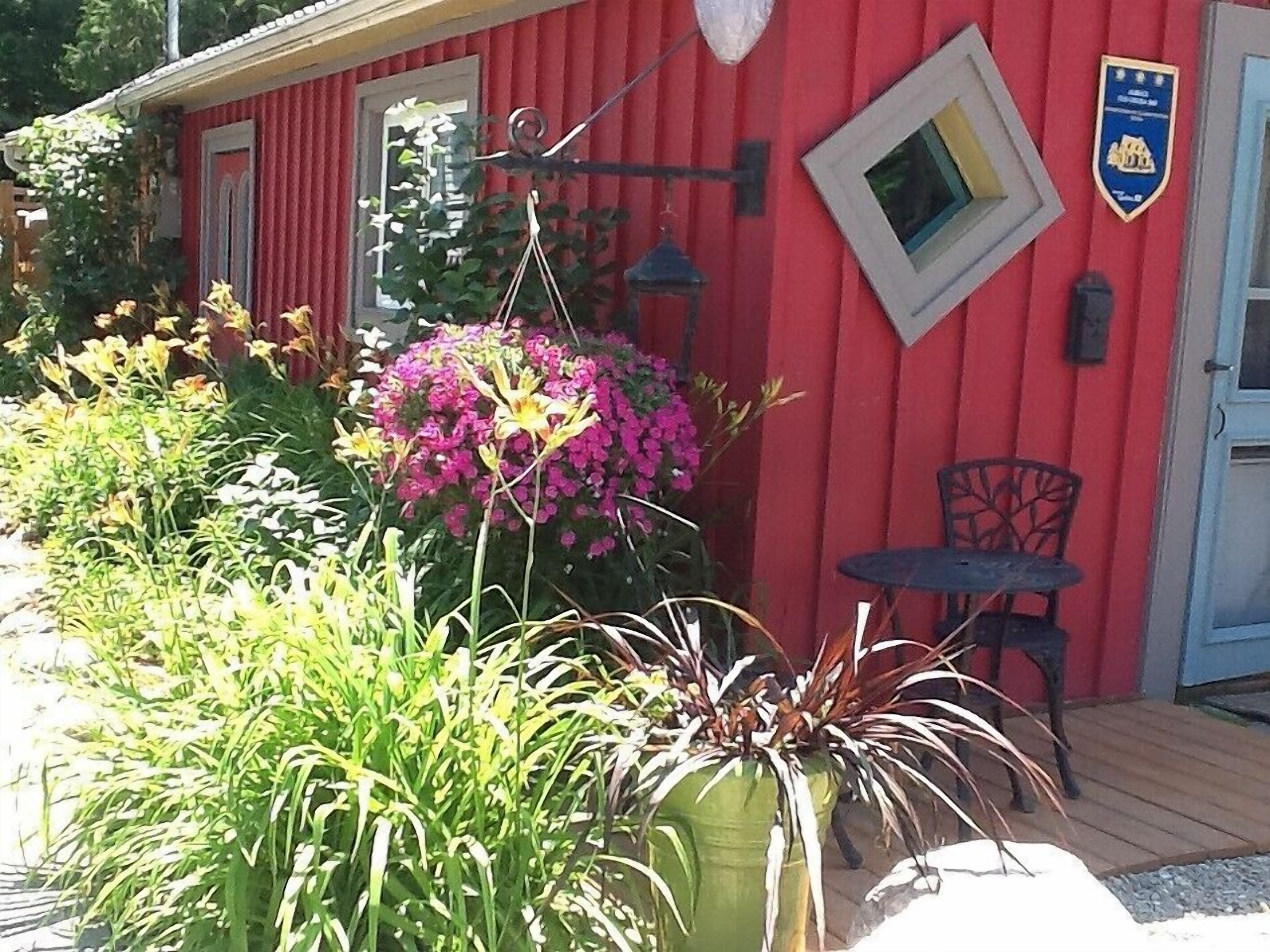 A red building with a window, a door, and a small table with a chair outside.