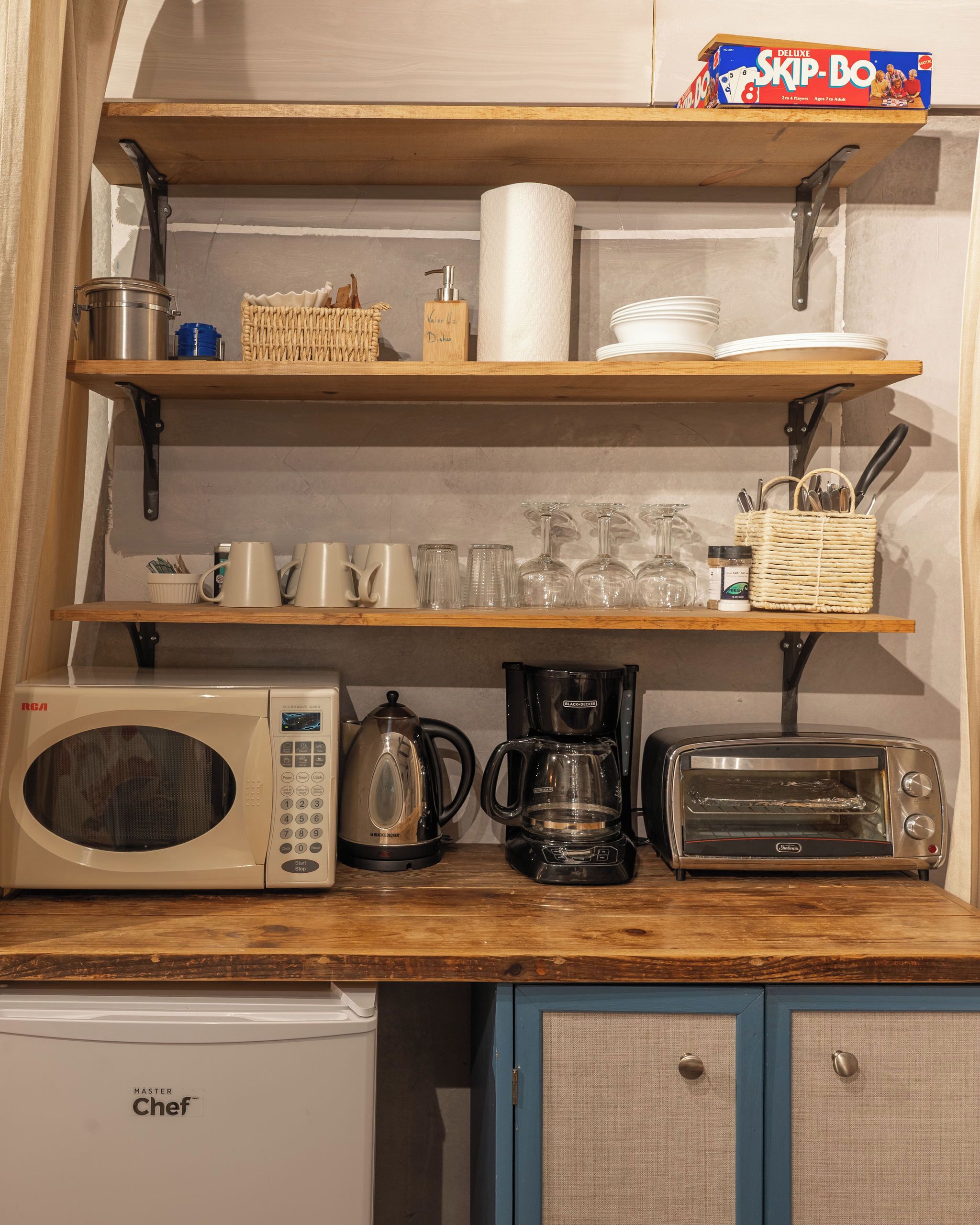 A kitchen with a microwave, coffee maker, toaster, and shelves with dishes and utensils.