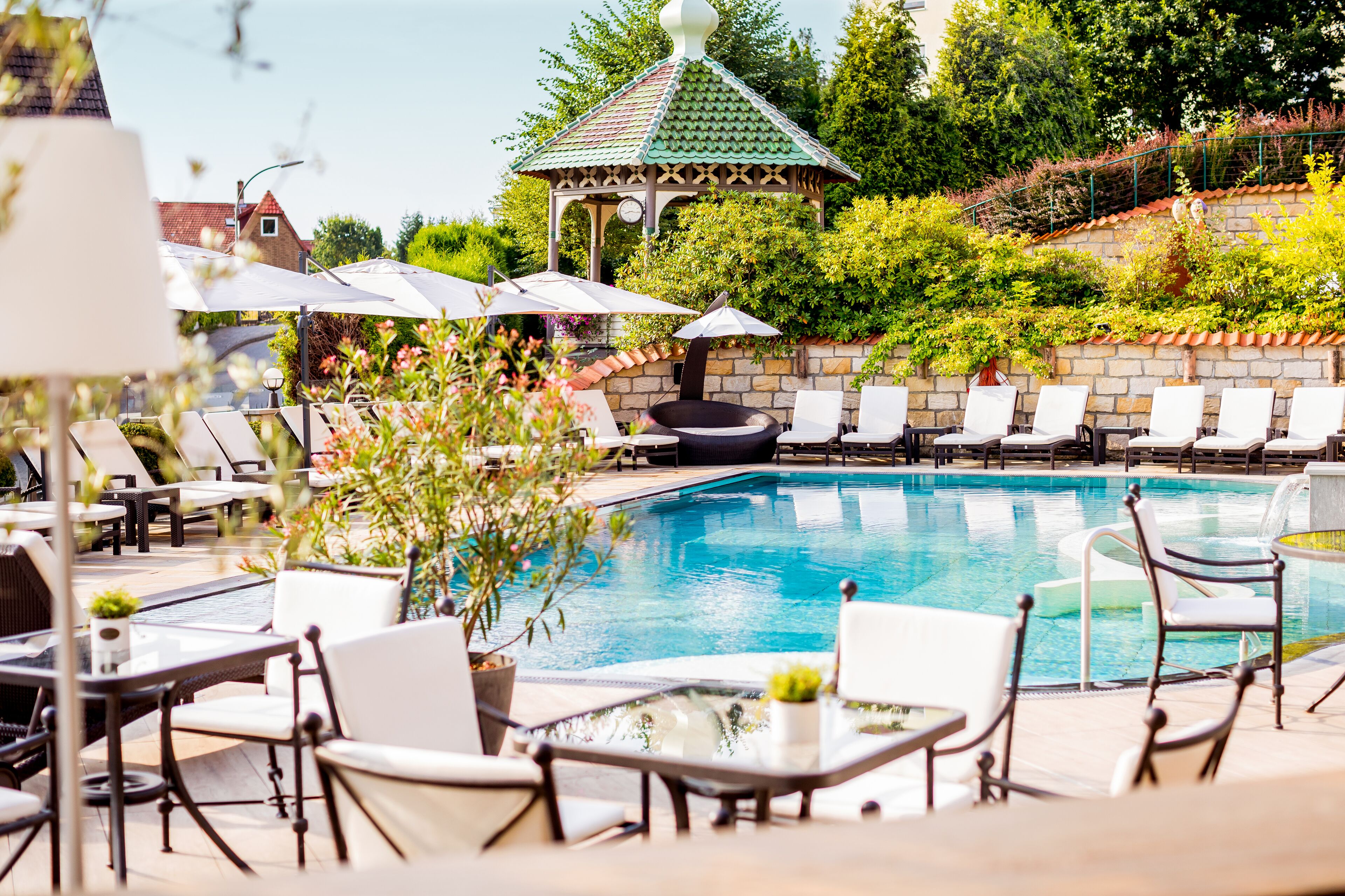 A pool area with lounge chairs, a gazebo, and a stone wall.
