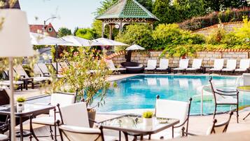 A pool area with lounge chairs, a gazebo, and a stone wall.