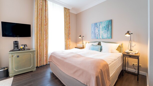 A hotel room with a bed, a television, a desk with a lamp, and a painting on the wall. - Romantischer Winkel RoLigio & Wellness Resort (Bad Sachsa)