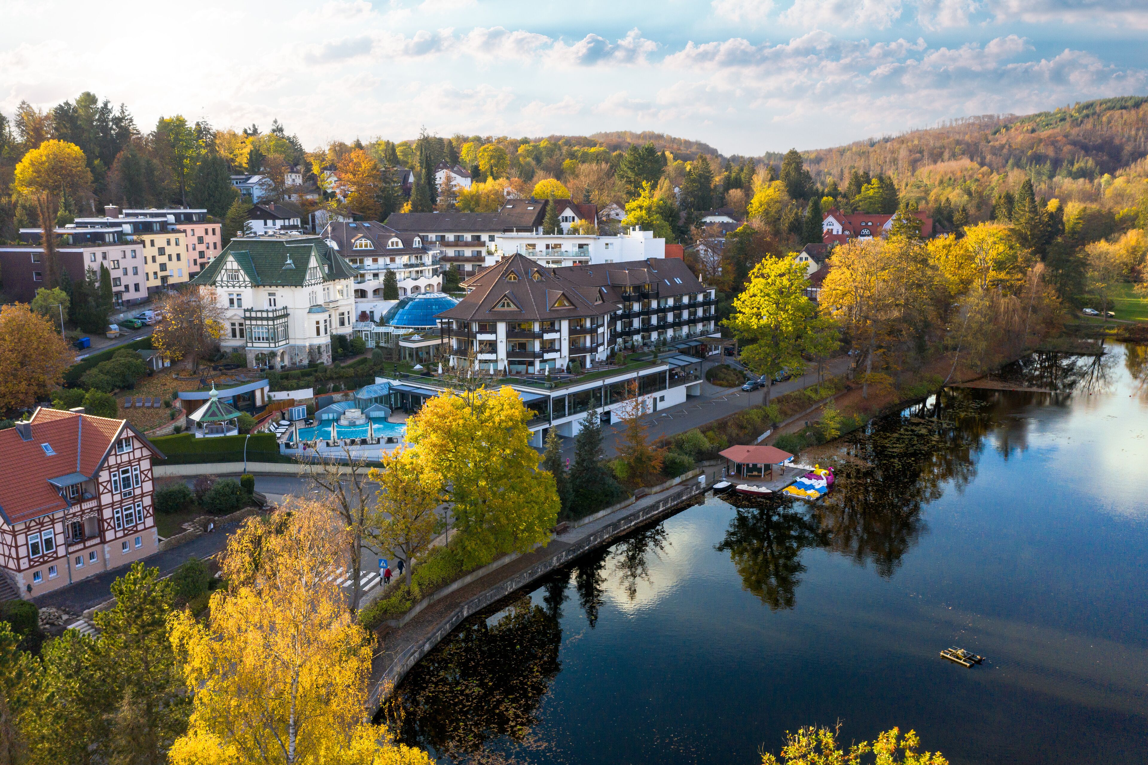 Un hôtel situé au bord de la rivière, composé de plusieurs bâtiments, avec un pont et entouré d’un feuillage automnal.