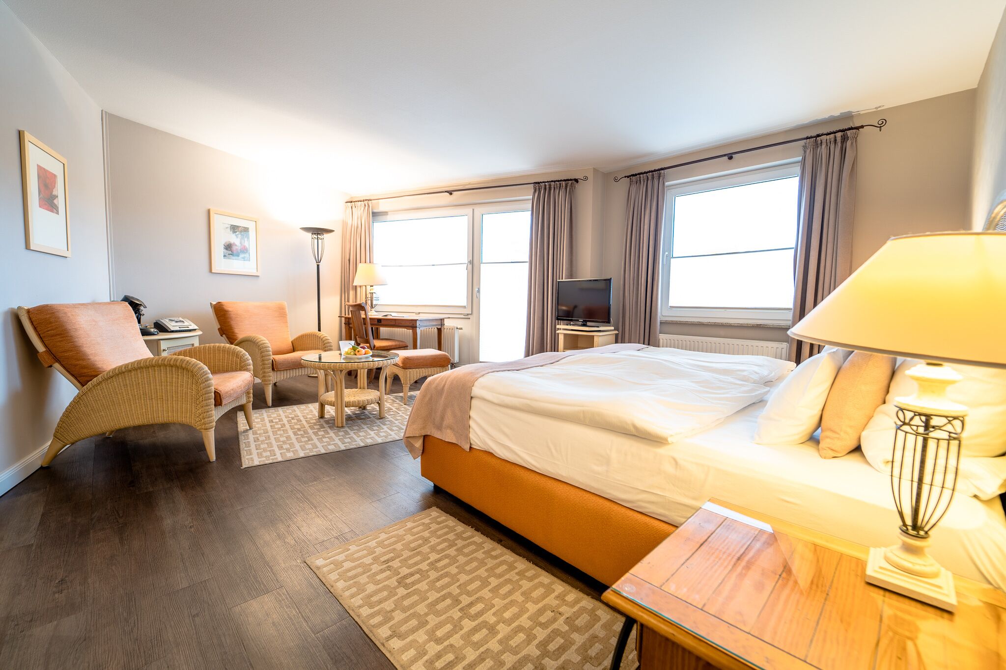 A hotel room with a bed, two armchairs, a small table, a TV, and a lamp.
