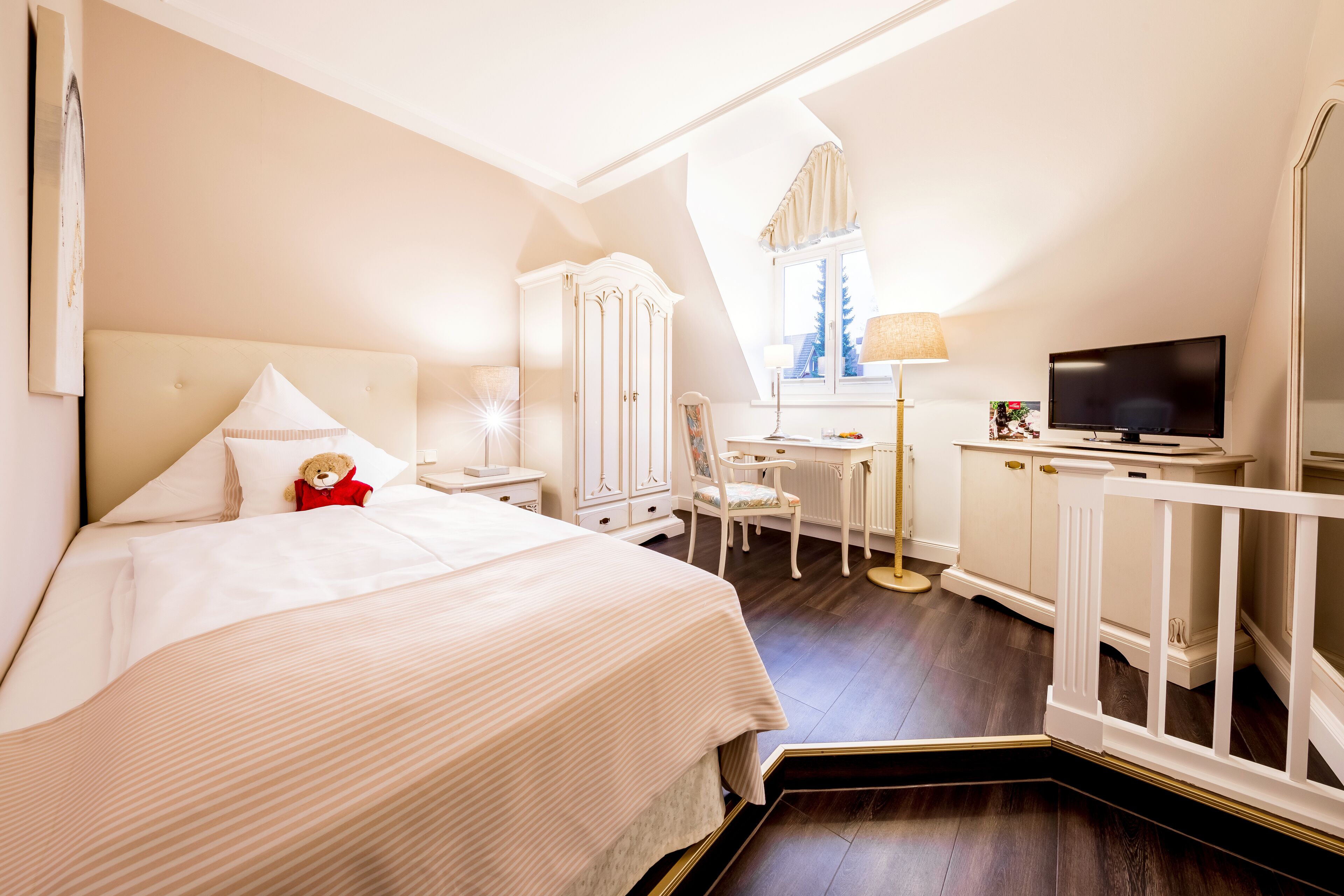 A hotel room with a large bed, a desk, a television, and a window with curtains.