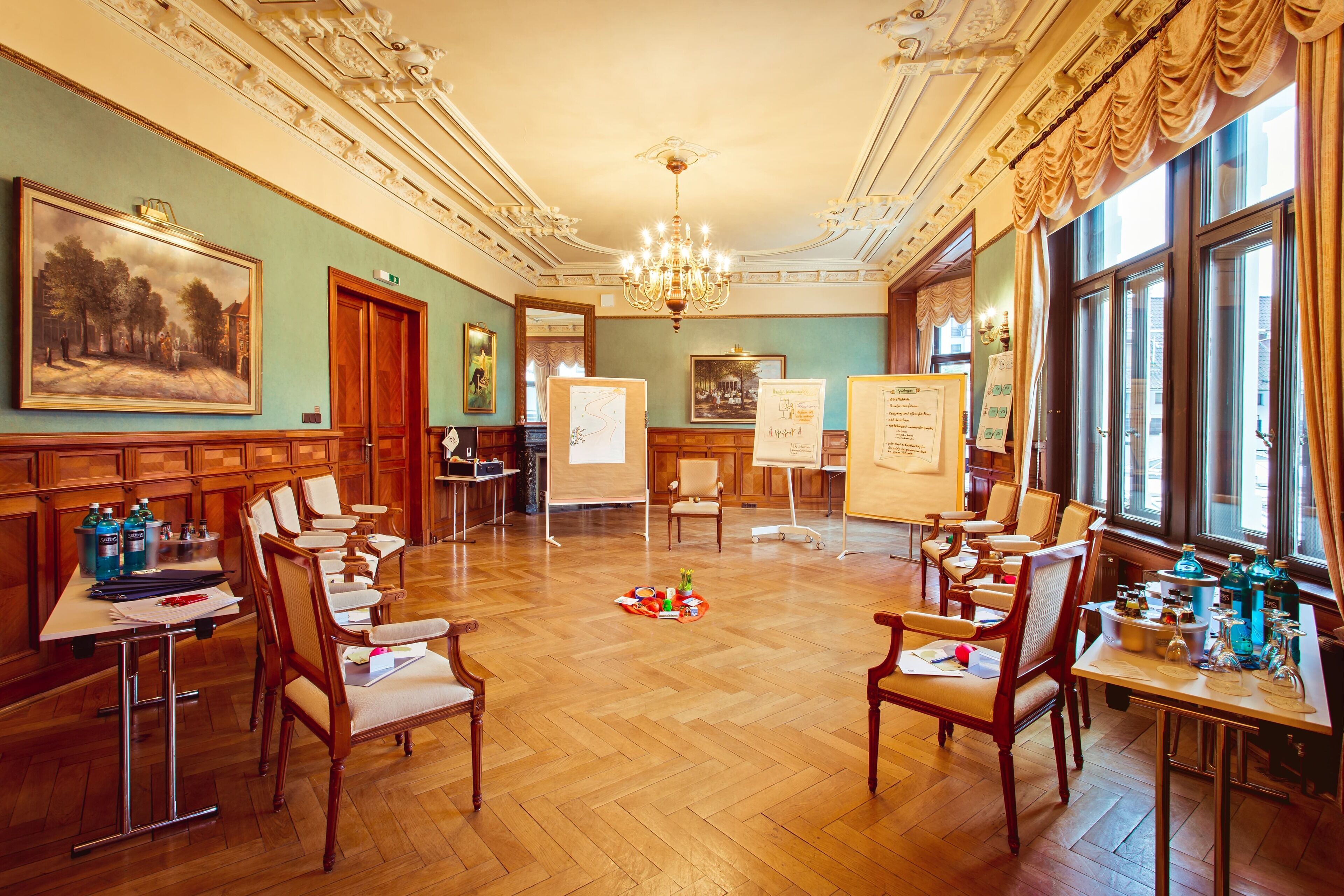 Une pièce spacieuse dotée de parquets en bois, de moulures décoratives au plafond et de grandes fenêtres avec des rideaux.