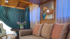 A cozy room with a wooden ceiling, a sofa with patterned cushions, a round table with a vase of flowers, and a chair. - Archontariki Boutique Hotel (Ioannina)