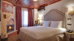 A hotel room with a large bed, a fireplace, a nightstand with a lamp, and a wall-mounted telephone. - Archontariki Boutique Hotel (Ioannina)