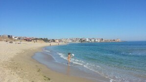 Una playa con cielo despejado, orilla de arena y edificios al fondo.