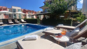 Una piscina con sillones de descanso y una mesa con una bebida.