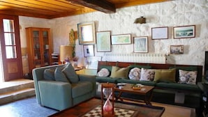 A cozy living room with a green sofa, a blue armchair, and a wooden coffee table. There is a bookshelf, a lamp, and framed pictures on the wall.