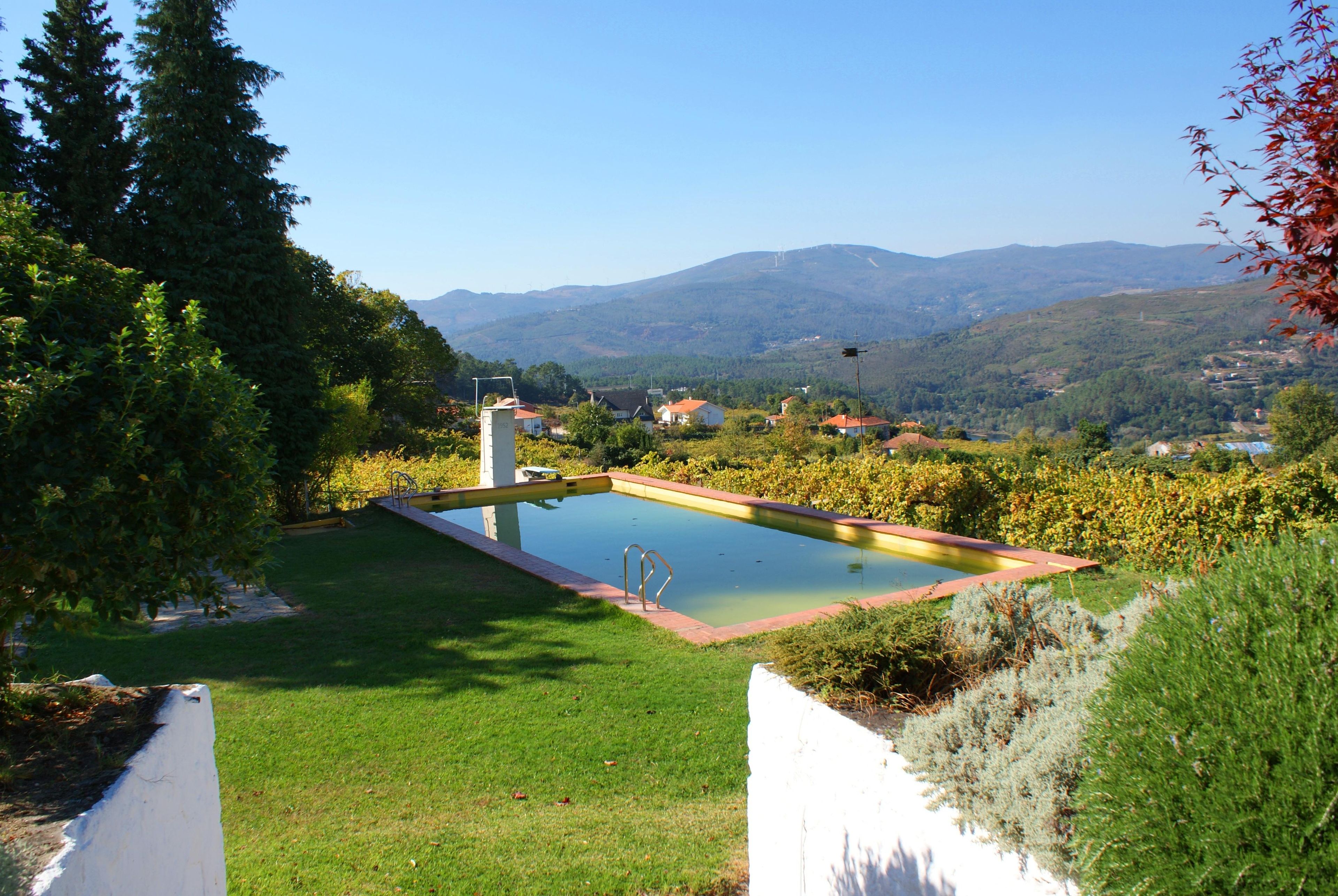 Una piscina rodeada de vegetación, con vistas a montañas y casas a lo lejos.