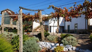 A traditional building with a stone facade, a wooden pergola, and a garden with various plants and a stone wall. - Quinta Da Calcada (Melgaço)