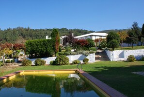 A residential area with a swimming pool, a white house, and a forested hill in the background. - Quinta Da Calcada (Melgaço)