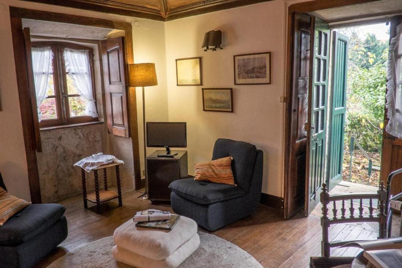 A cozy room with a wooden floor, a dark armchair, a small table with a lamp, and a window with curtains.