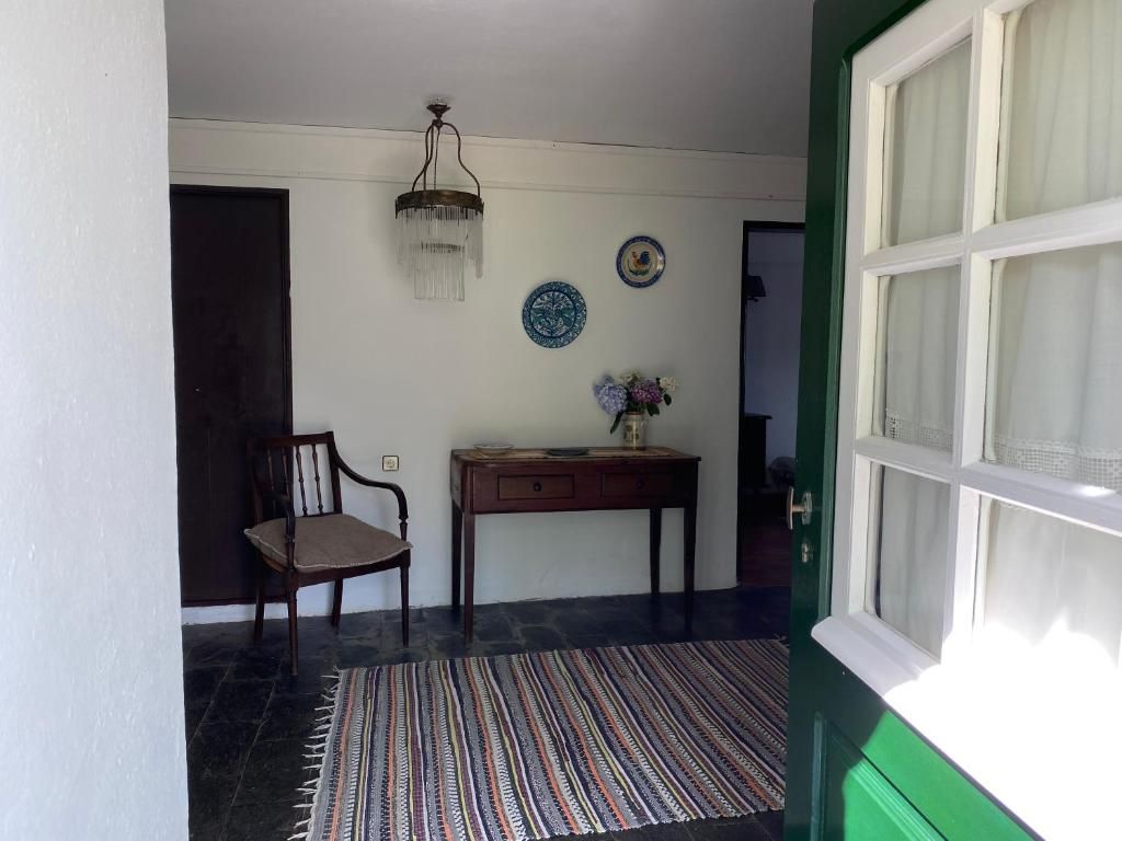 A room with a wooden chair, a small table with a vase, a patterned rug, and a green door.