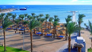 A beachside resort with rows of sun loungers and umbrellas, a pier extending into the sea, and several boats in the background. - Pickalbatros Palace Hurghada (Hurghada)