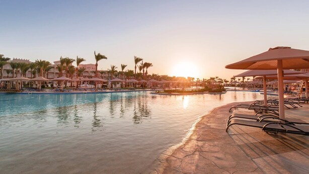A resort pool area with lounge chairs and umbrellas, surrounded by palm trees and hotel buildings. - Pickalbatros Palace Hurghada (Hurghada)