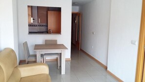 A modern living room with a beige sofa, a wooden dining table, and a kitchen area with cabinets and a sink. - Benicarlo 3000 (Benicarlo)
