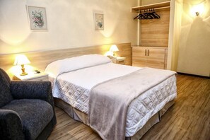 A hotel room with a bed, bedside lamps, a chair, a wardrobe, and a wall-mounted coat rack. - SAN Silvestre (Tubarao)