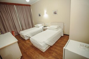 A hotel room with two beds, a desk, a chair, and a small refrigerator.