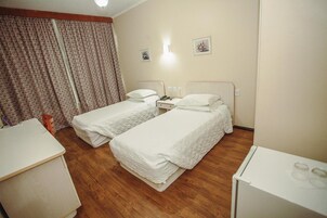 A hotel room with two beds, a desk, a chair, and a small refrigerator.