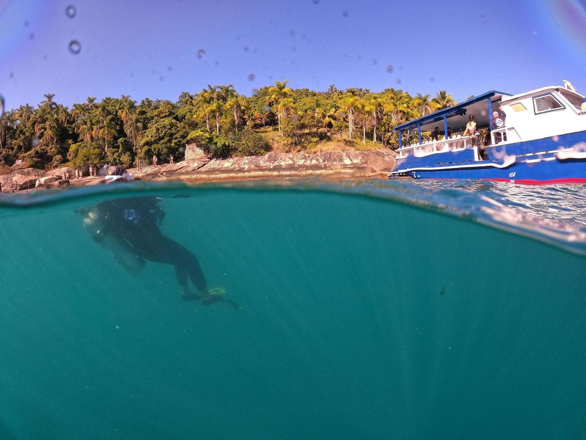 A diver swimming in clear turquoise water near a boat with a blue and white color scheme.
