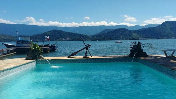 A clear blue pool with a view of mountains and a dock with boats. - Aquamaster Dive Pousada (Angra dos Reis)