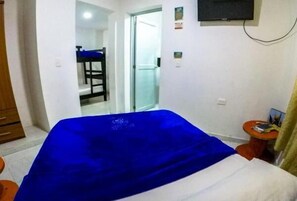 Une chambre d’hôtel avec un lit, une petite table, une chaise et un téléviseur fixé au mur.