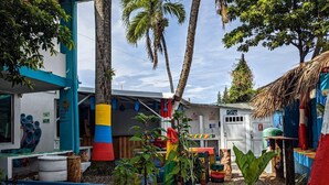Un espace extérieur coloré avec un parterre de fleurs peint en bleu, un bâtiment blanc avec une enseigne et un palmier.