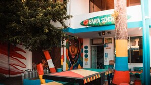 Un espace extérieur coloré, aménagé avec des sièges et agrémenté d’une fresque murale ainsi que d’une enseigne sur laquelle on peut lire « BAHIA SONORO ».